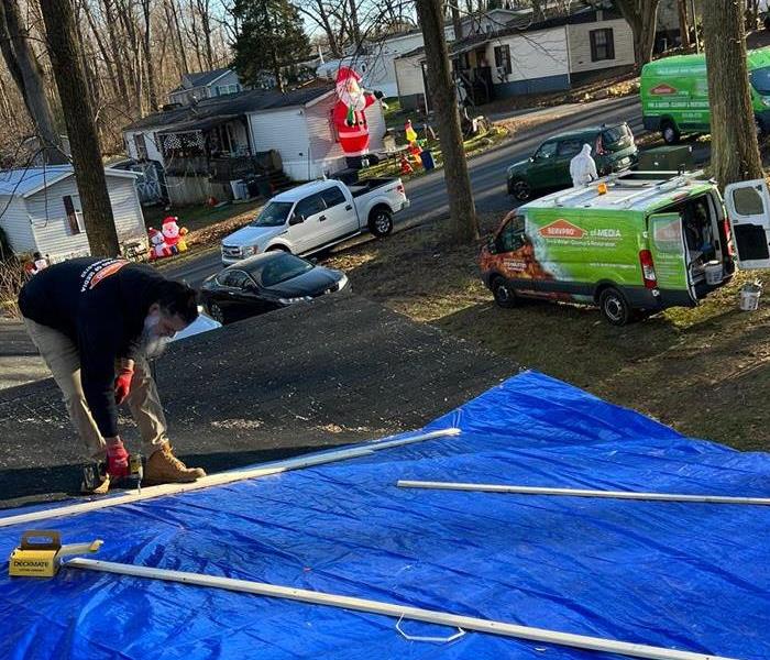 This image is of one of our team members tarping up a roof that was damaged by a tree during a storm